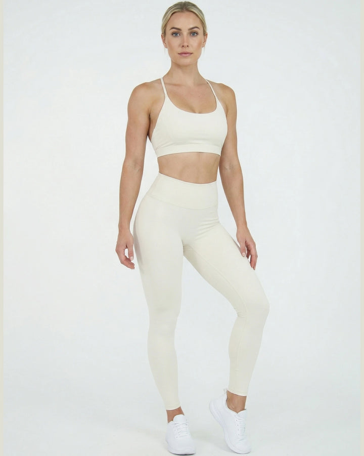 Woman wearing a white sports bra and leggings set on a white background