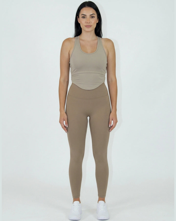 Woman wearing a beige tank top and leggings on a white background