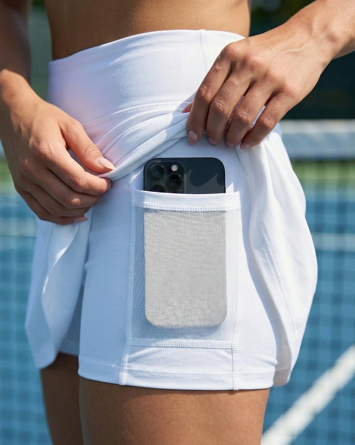 Person wearing white shorts with a pocket holding a phone and towel, against a blurred poolside background.