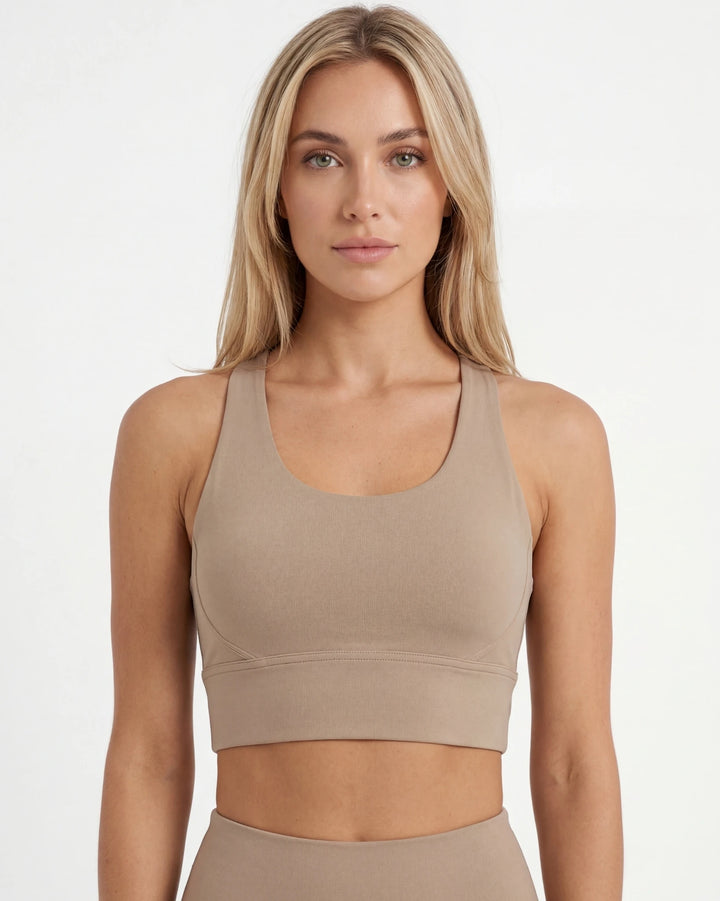 Woman wearing a beige sports bra and leggings on a white background
