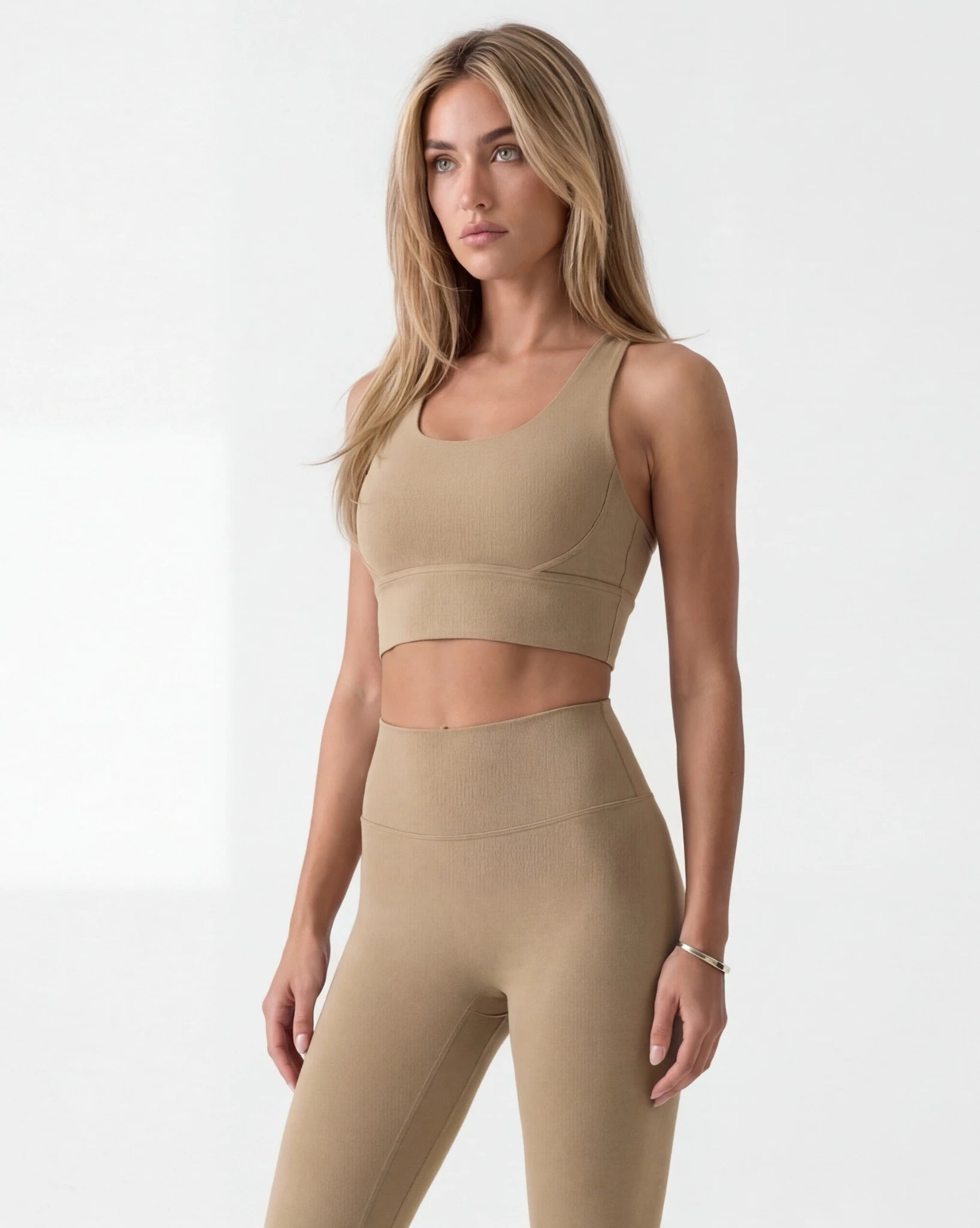 Woman wearing a beige sports bra and leggings set on a white background