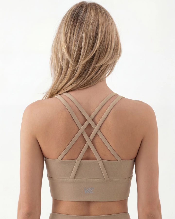 Beige sports bra with criss-cross straps worn by a person on a white background