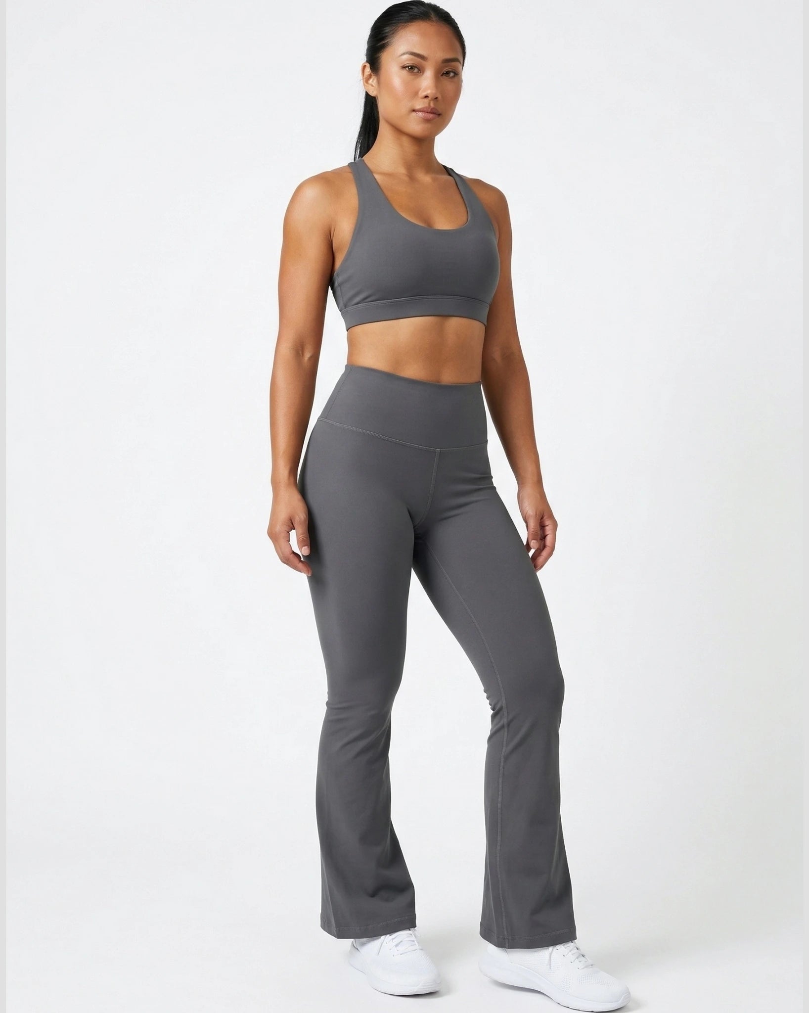 Woman wearing a gray sports bra and leggings set on a white background