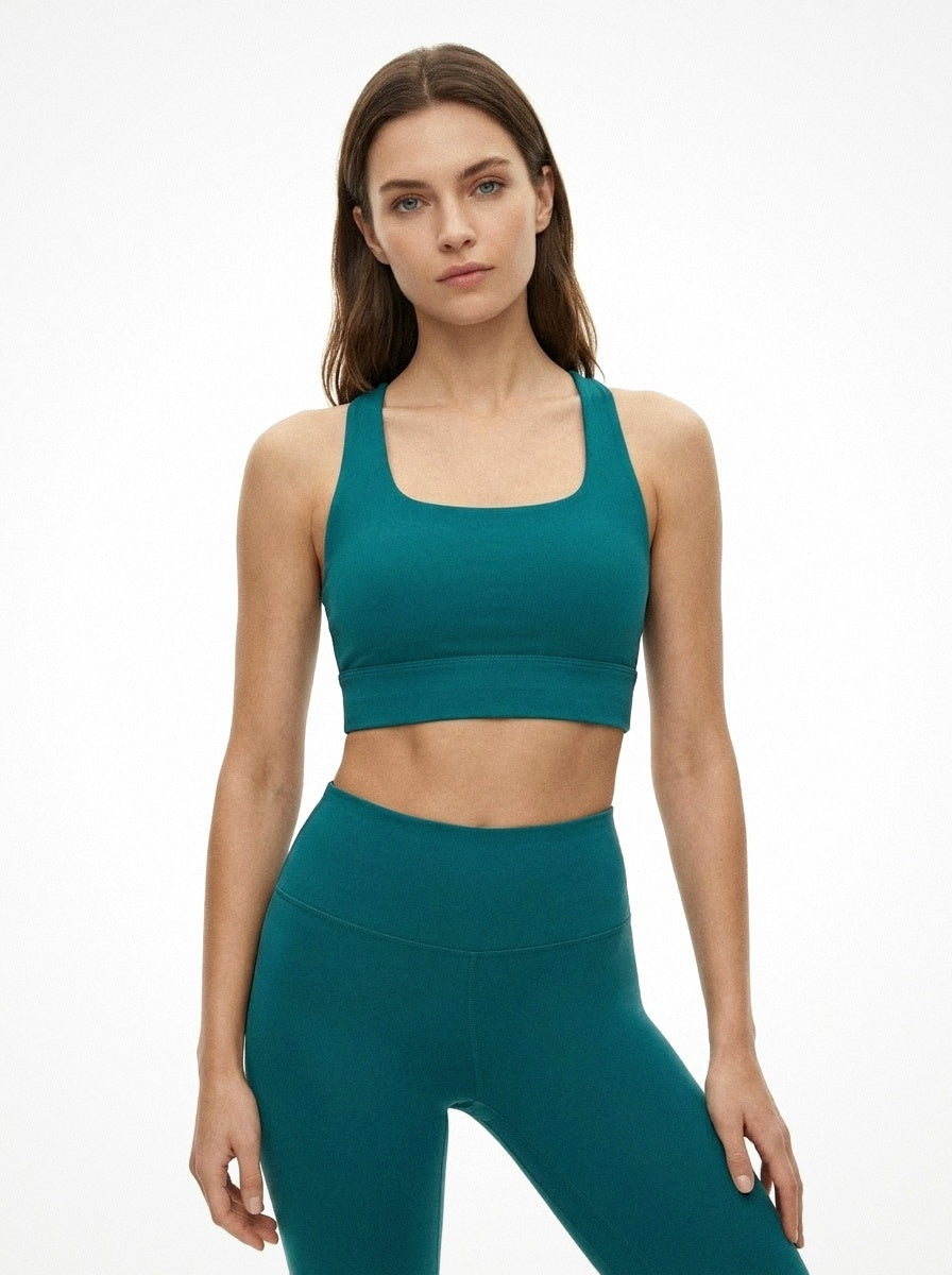 Woman wearing a teal sports bra and leggings on a white background